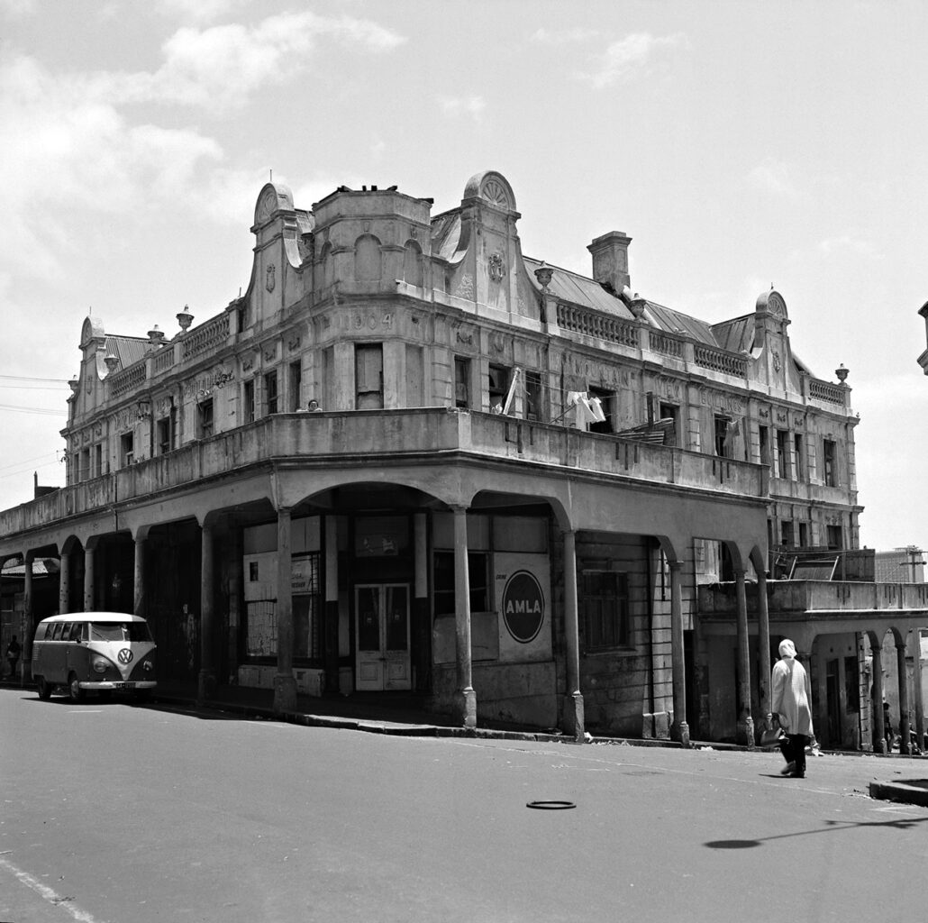 Woman walking across the road towards an old corner building. District Six, Cape Town.