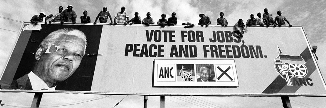 Gallery F - Keith Bernstein Nelson Mandela A billboard of Nelson Mandela. A group of young men standing on top of the billboard.
